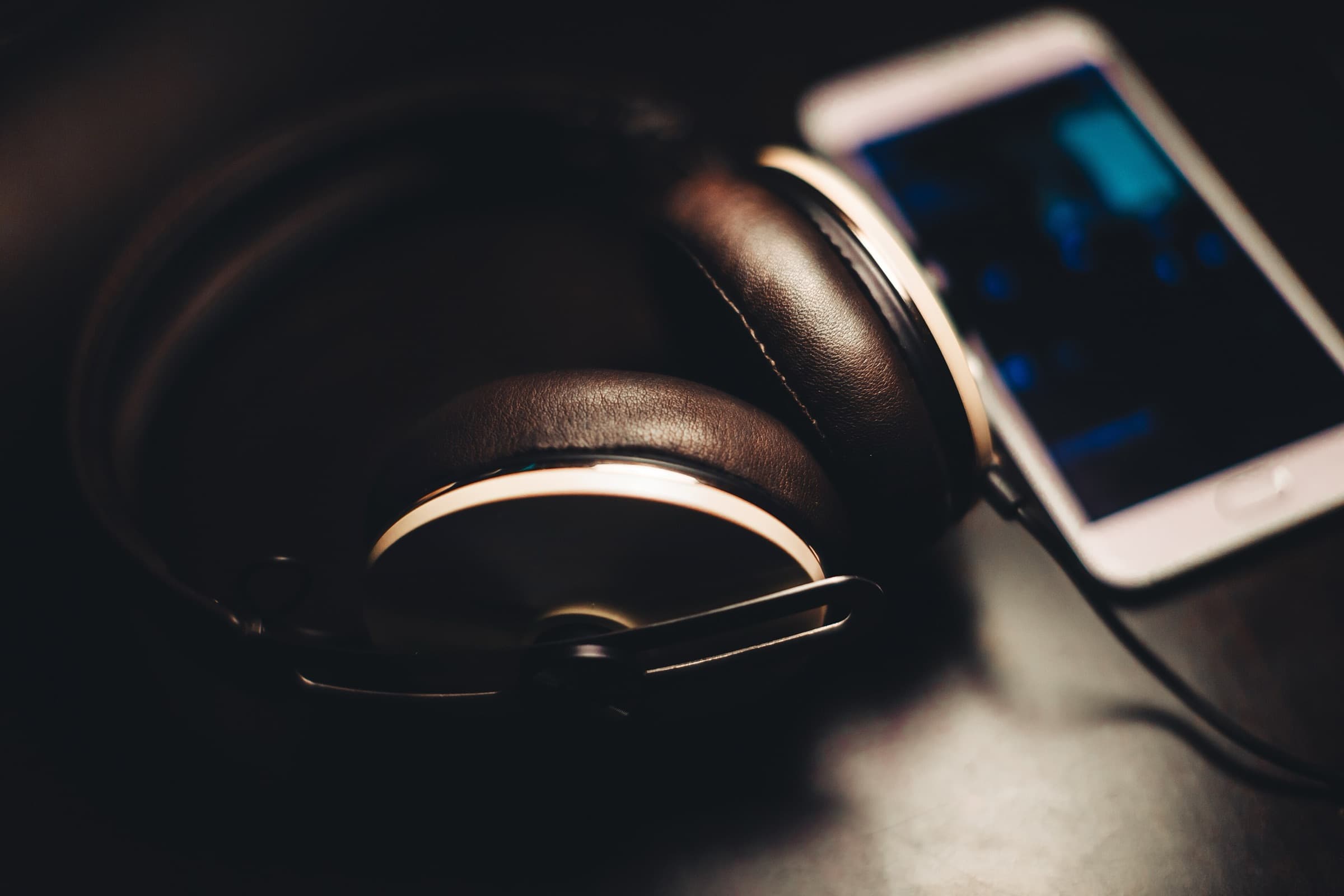 Leather headphones beside a smartphone with a glowing screen